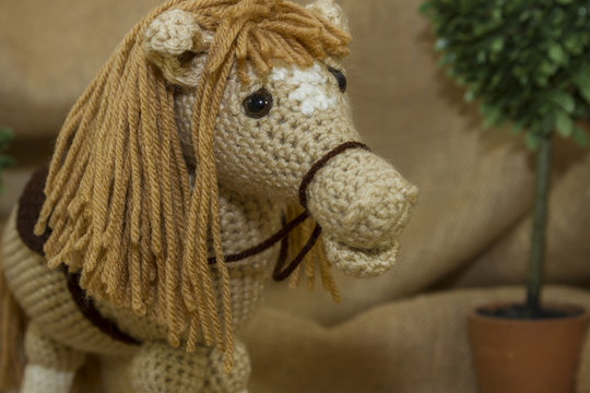 A close-up image of a handmade crocheted toy horse photographed on a rustic burlap background.