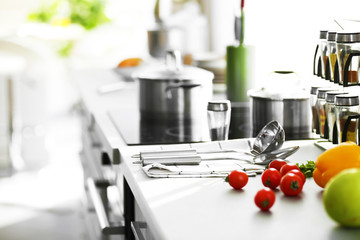 Modern table and electric stove with utensils and vegetables in the kitchen beside window