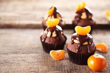 Tasty cupcakes with slice of mandarin and chocolate on wooden background