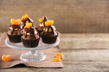 Tasty cupcakes with slice of mandarin and chocolate on wooden background