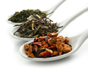Different sorts of dry tea in ceramic spoons, isolated on white