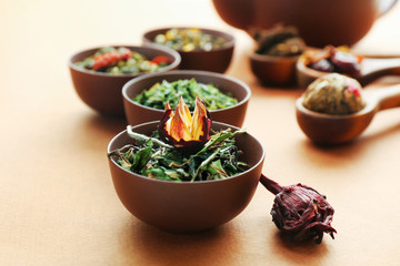 Variety of dry tea in bowls with teapot on light brown background, closeup