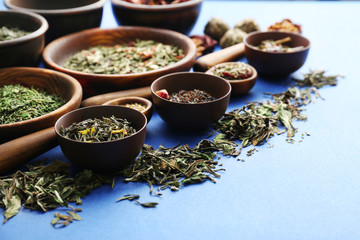 Variety of dry tea in bowls and wooden spoons on blue background, closeup