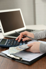 Woman making calculations while holding dollar bills over tax form on the wooden table, close up