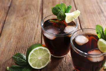Two glasses of cola with ice, mint and lime on wooden table background