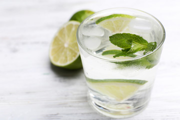 Fresh cocktail with ice, mint and lime on white wooden table background