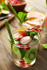 Refreshing cocktails with ice, mint, pomegranate seeds and slices of fruits on wooden background