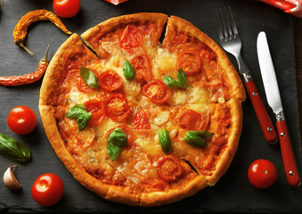 Margherita pizza with utensils and vegetable on slate plate