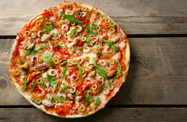 Pizza with seafood, red pepper and green olives on wooden table