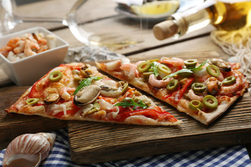 Pizza slices with seafood, red pepper, green olives and bottle of wine on wooden table