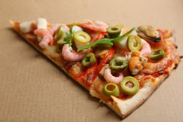 Pizza slice with seafood, red pepper and green olives on cardboard background