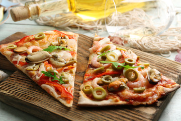 Pizza slices with seafood, red pepper, green olives and bottle of wine on wooden table