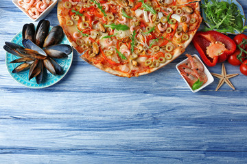 Pizza with seafood, red pepper and green olives on blue wooden table