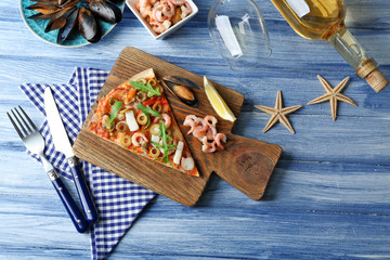 Pizza slice with seafood, red pepper, green olives and bottle of wine on blue wooden table