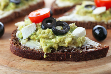 Avocado sandwiches with tomatoes and olives on cutting board