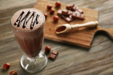 Glass of chocolate milkshake and nuts on wooden background