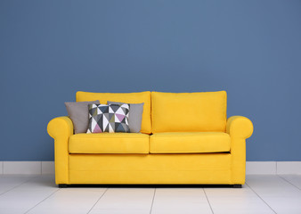 Yellow sofa and multicoloured pillows on a blue wall background