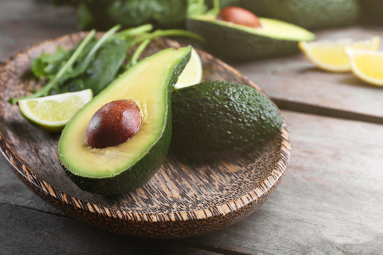 Sliced avocado with lime, spinach and arugula on wooden plate