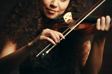 Beautiful young woman playing violin over brick wall background