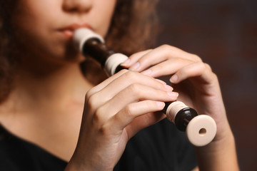 Beautiful young woman playing on recorder over brick wall background