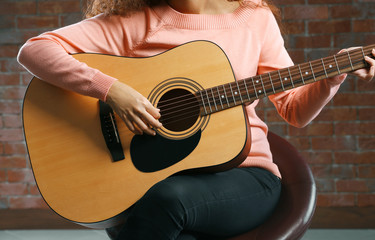 Obraz premium Beautiful young woman playing on guitar over brick wall background