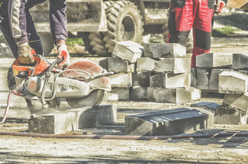 Worker cutting concrete curb at reconstruction area with machinery in background