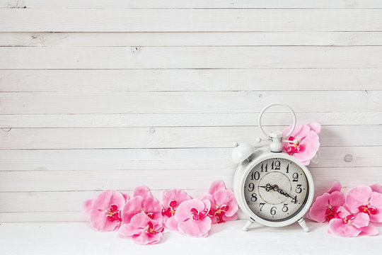 Background with white alarm clock and flowers pink orchid on whi