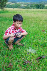 Young boy exploring nature with magnifying glass. Outdoors in the day time.