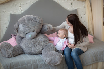mother with her baby daughter playing with big toy bear in a rea