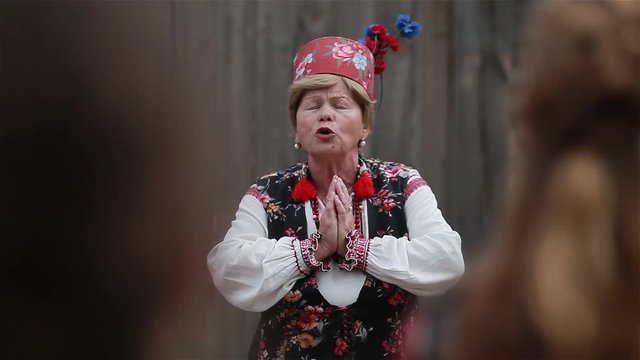 Old lady in a traditional Slavic clothing explaining customs and rituals of rural style wedding. Close up