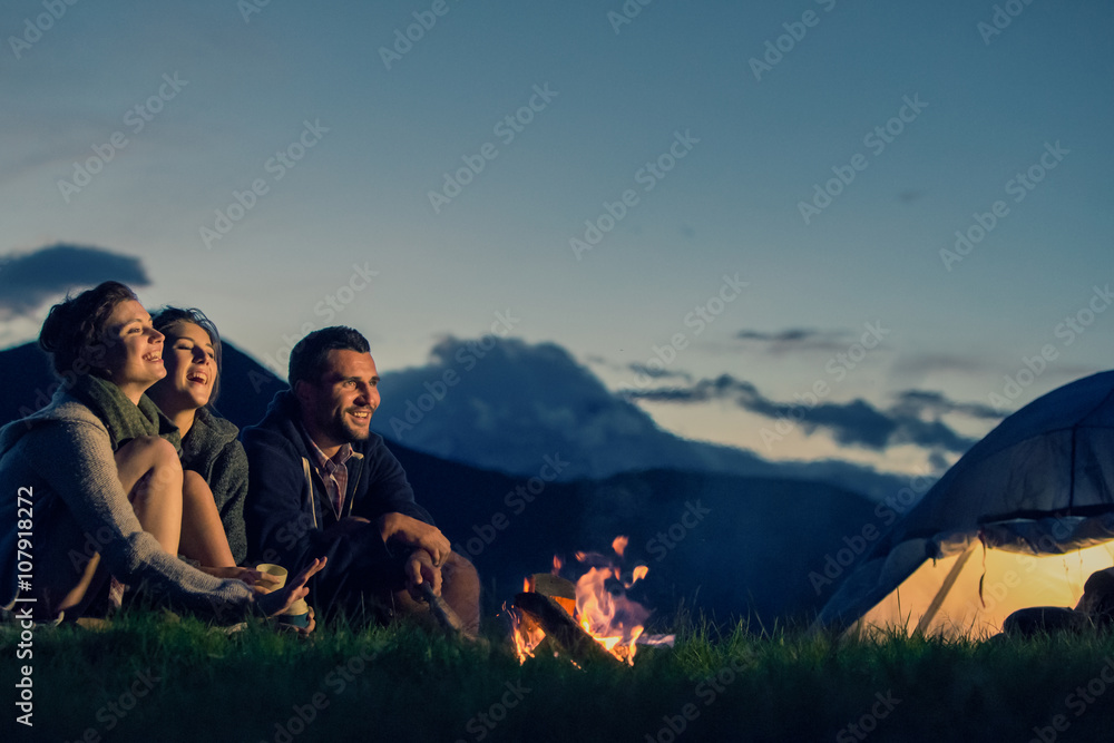 Wall mural three friends camping with fire on mountain at sunset