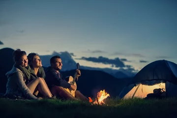 Wall murals Camping Three friends camping with fire on mountain at sunset