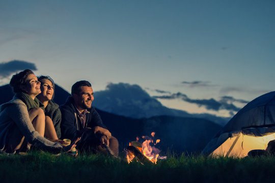 Three friends camping with fire on mountain at sunset