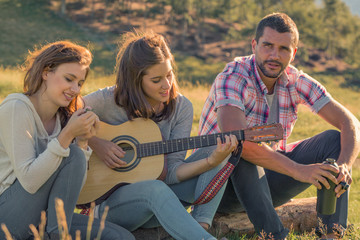 Young woman sing playing guitar with friends on sunset outdoor