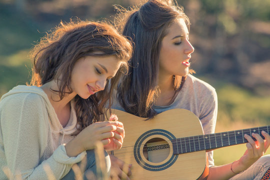Young woman sing playing guitar with friend on sunset outdoor