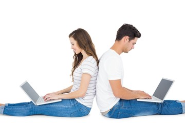 Happy couple sitting on the floor back to back using laptop