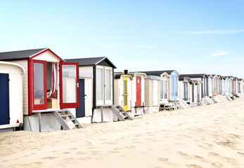 Beach huts or houses and blue sky. Multicolored beach bathing huts with white sand and clear blue sky. Beach scene with copy space. Side view of beach huts in a row.