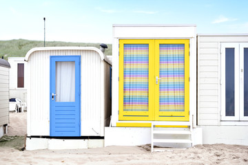 Beach huts or houses and blue sky. Multicolored beach bathing huts with white sand and clear blue sky. Beach scene with copy space. Front view of beach huts in a row.