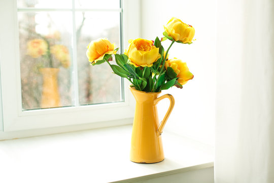 yellow flowers in a yellow vase on a windowsill