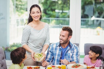 Smiling mother standing at dining table with family 