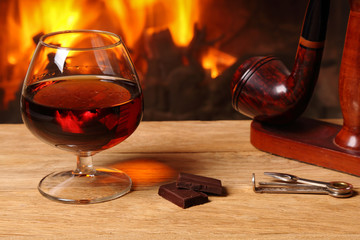 A glass of brandy, chocolate and tobacco pipe  on the background