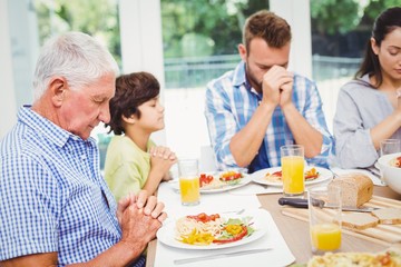 Multi generation family praying while sitting at dining table 