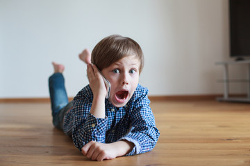 Naklejka premium funny boy lying on the wooden floor and speaking mobile phone 