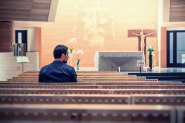 Young beared man wearing blue shirt praying in modern church