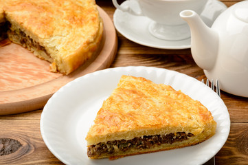 Piece of pie with minced meat on wooden table.