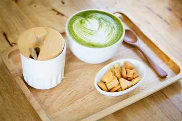 White cup  of green tea on a wooden tray with a snack