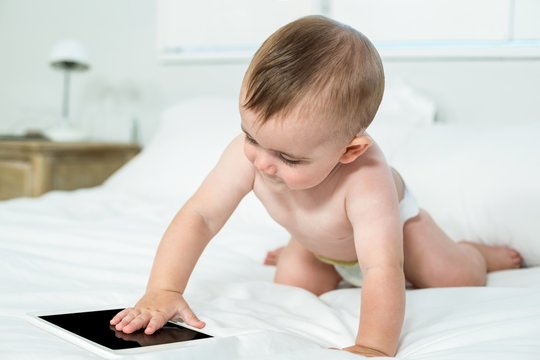 Baby boy touching digital tablet on bed at home