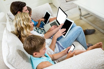 Family using various technologies while sitting on sofa
