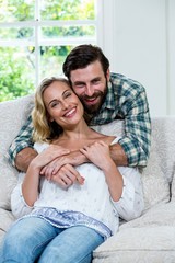 Young man embracing wife from behind against window