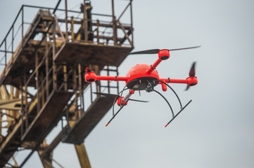 Red industrial drone flies over metal structures industrial faci